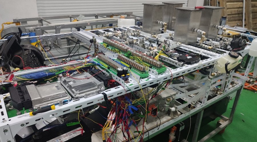 Bench photograph of a hardware-in-the-loop test rig: an aluminium frame carrying power electronics, current sensors, coolant lines and dense wiring harnesses.